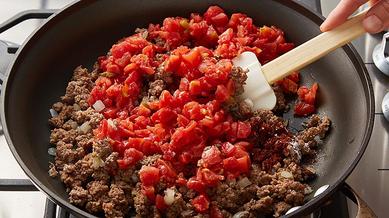 Brown ground beef, onion, and tomatoes in a skillet.