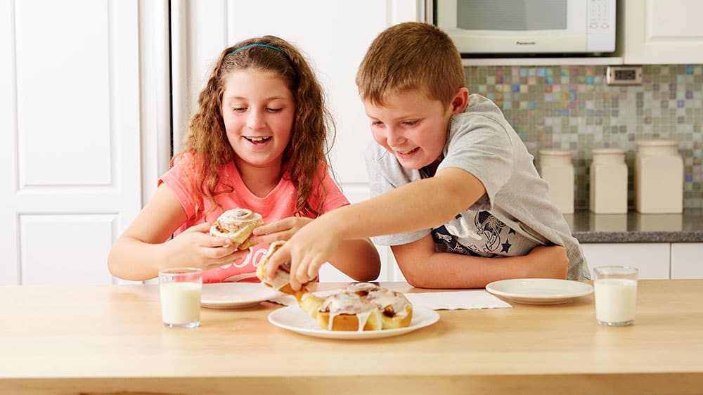 Two kids eating cinnamon rolls