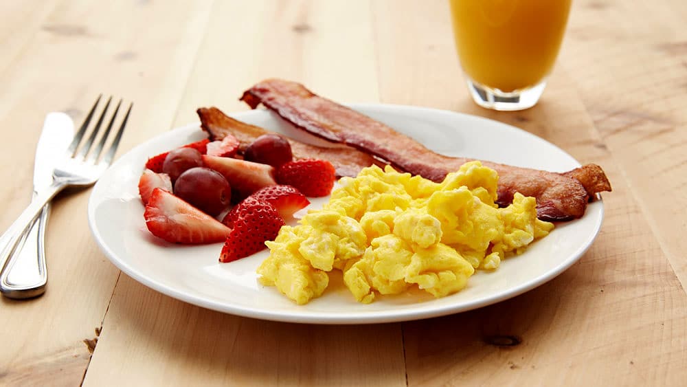 Scrambled eggs, bacon, fruit, juice