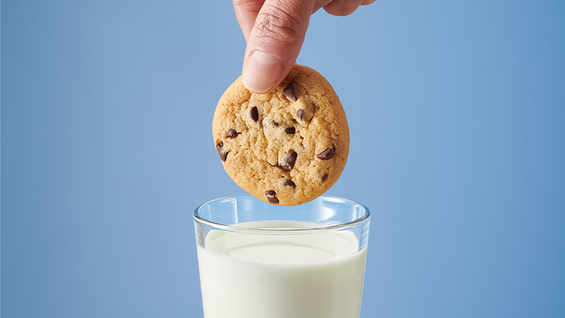 Pillsbury Soft Baked Chocolate Chip Cookie being dunked in a glass of milk