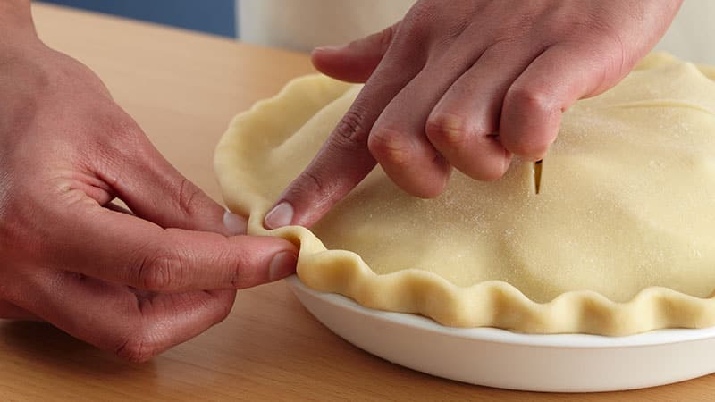 Place your thumb and index finger about an inch apart on the outside of the raised crust edge. With your other index finger, push the pastry toward the outside to form a scalloped edge.