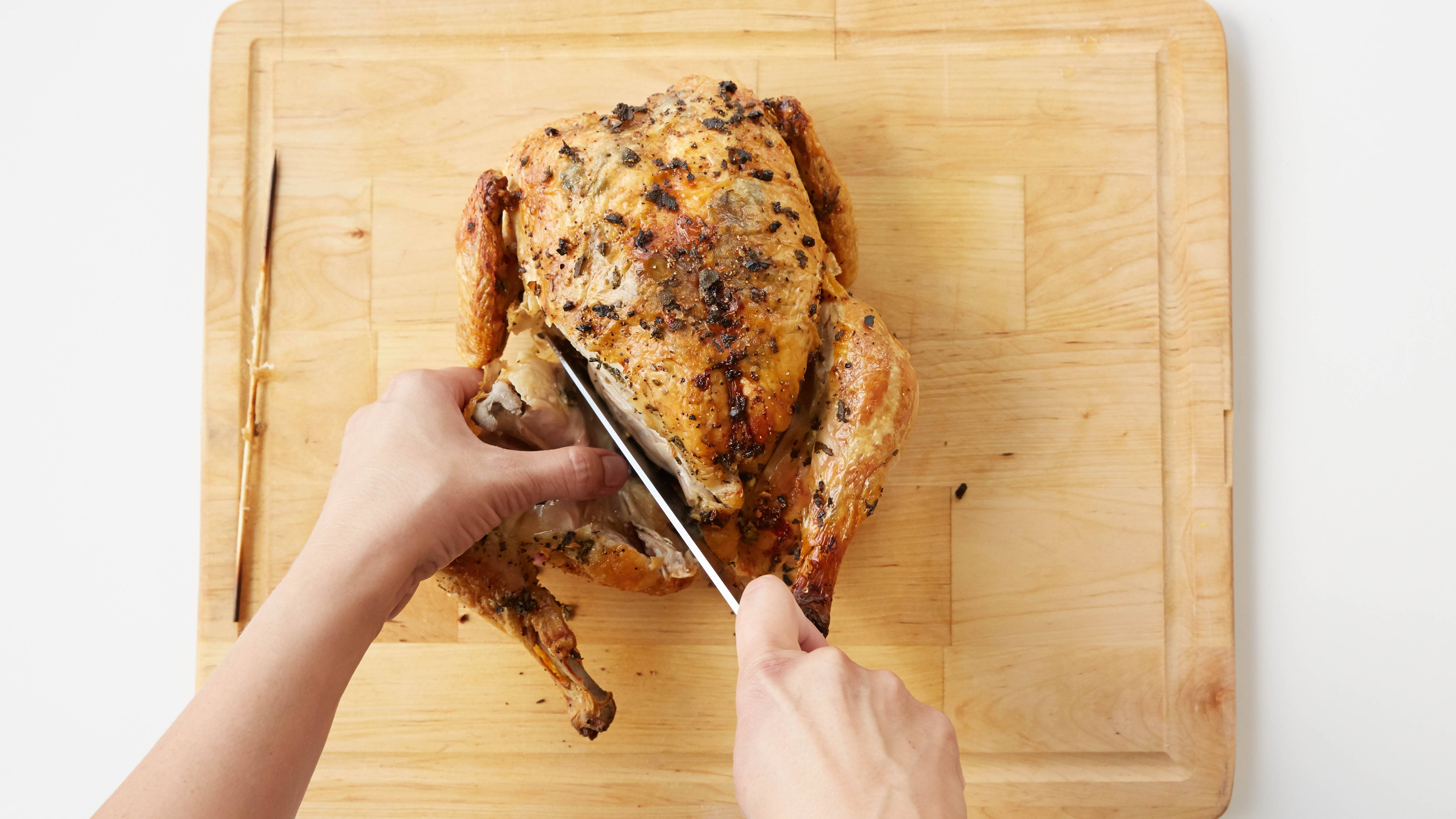 A person carving a cooked chicken on a cutting board