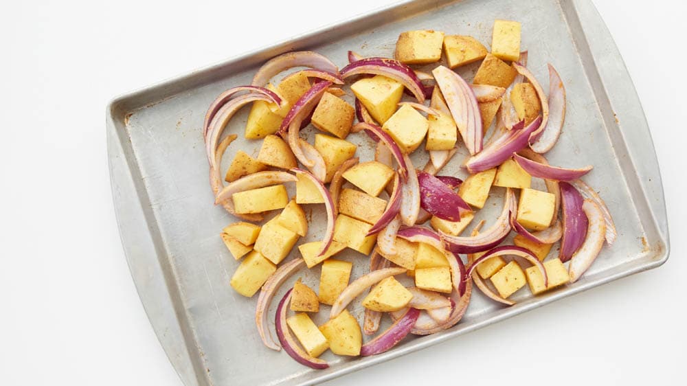 Cubed yukon gold potatoes, sliced red onion on a baking sheet