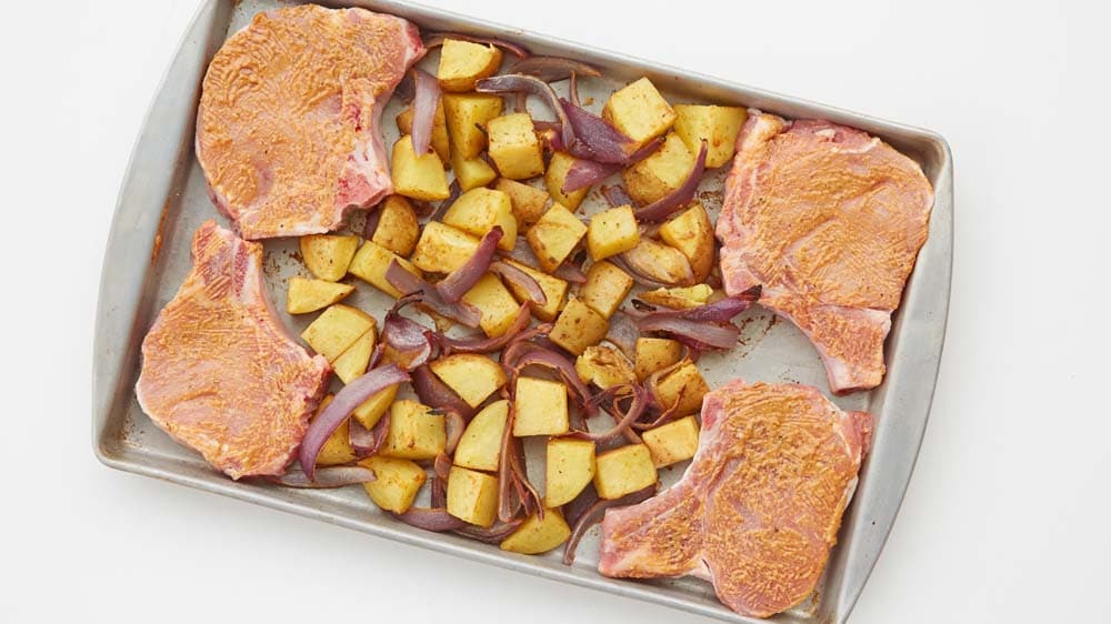 Cubed yukon gold potatoes, sliced red onion and pork chops on a baking sheet