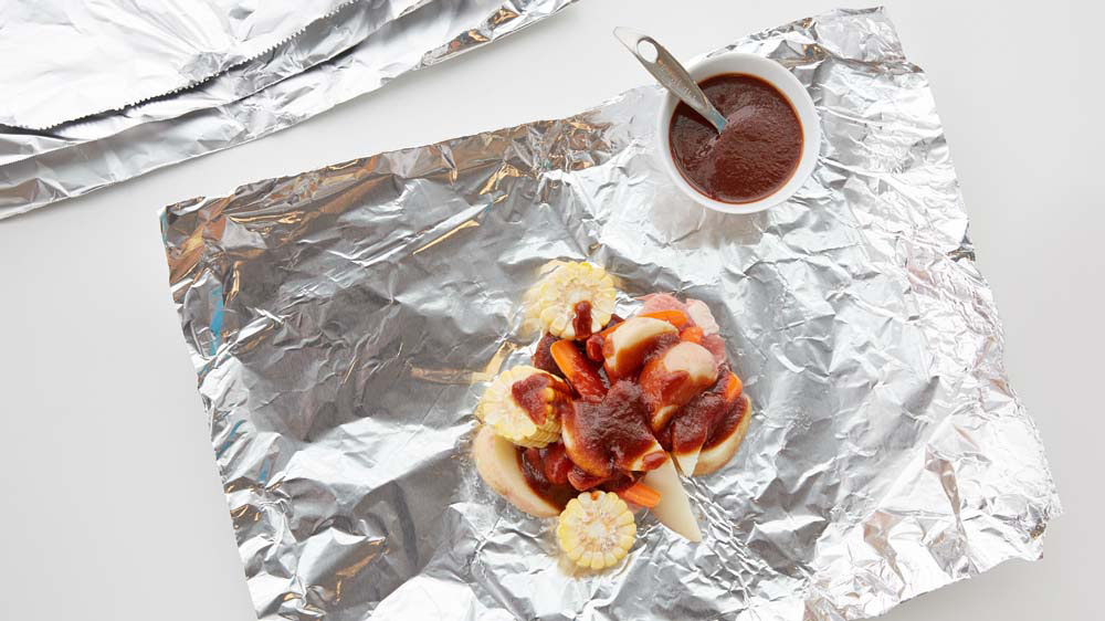 Pork chop, corn, carrots, potato wedges and barbecue sauce on foil