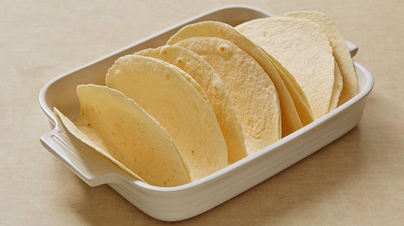 Fold the flour tortillas in half and place folded-side-down in baking dish.