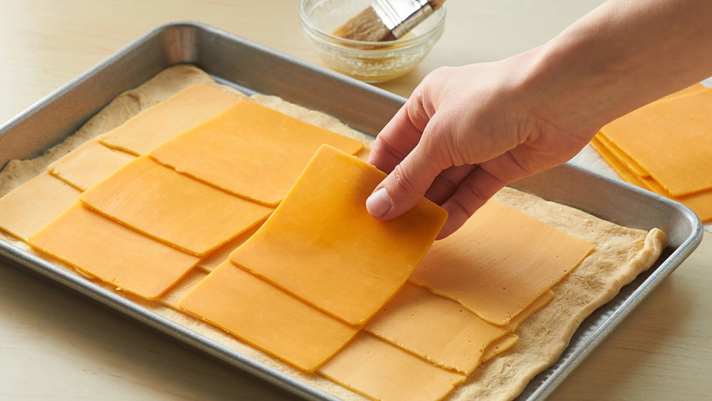 Layer both the American and Cheddar cheeses onto the dough leaving a 1/2-inch border around the edges. 