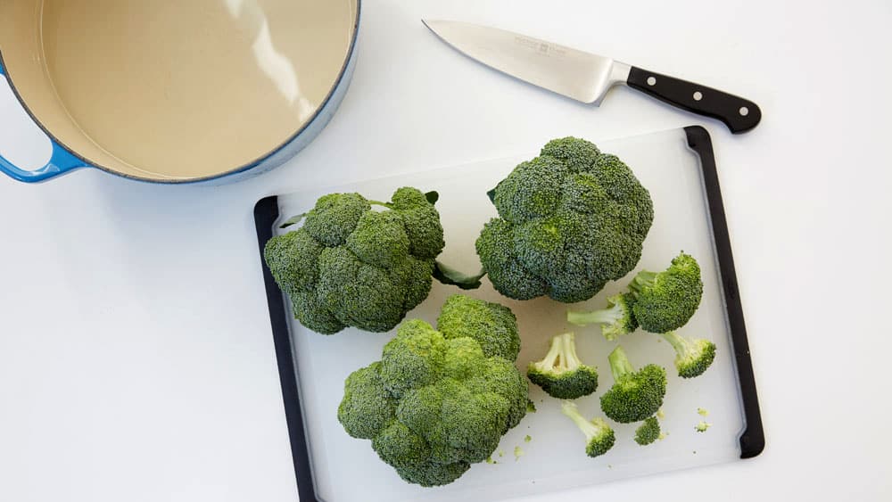Broccoli on a cutting board with a pot and a knife