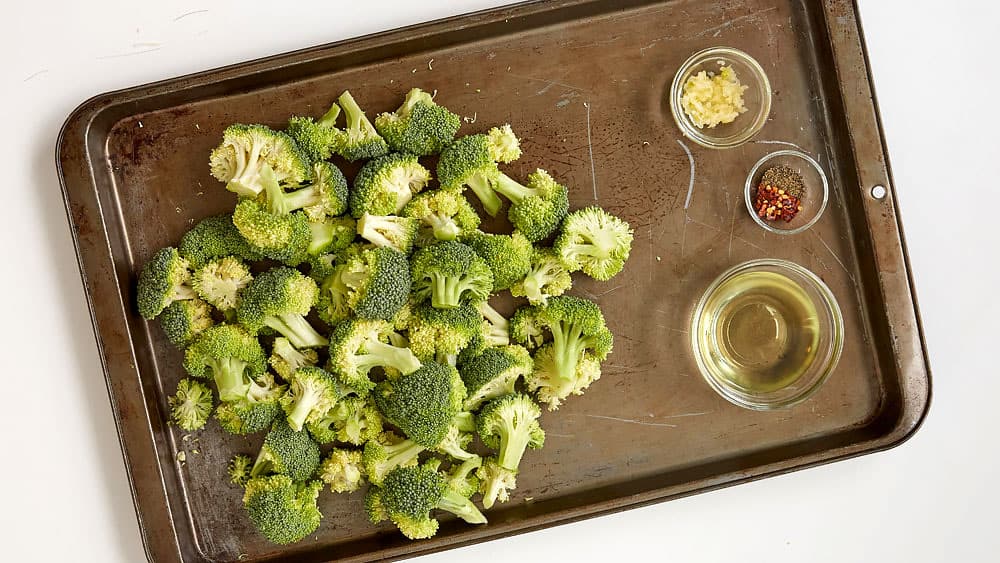 Broccoli florets, garlic, olive oil, salt, pepper, red pepper flakes on a 15x10x1 inch baking sheet