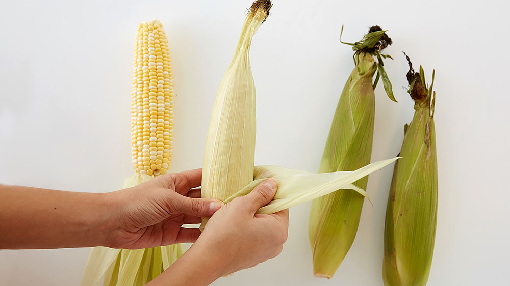 First, peel back the husk leaves one at a time until only a thin layer of leaves remain around the corn. 