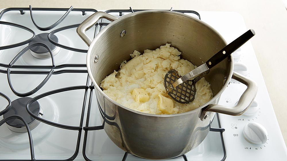 Mashed potatoes, milk, potato masher in a pan on the stove