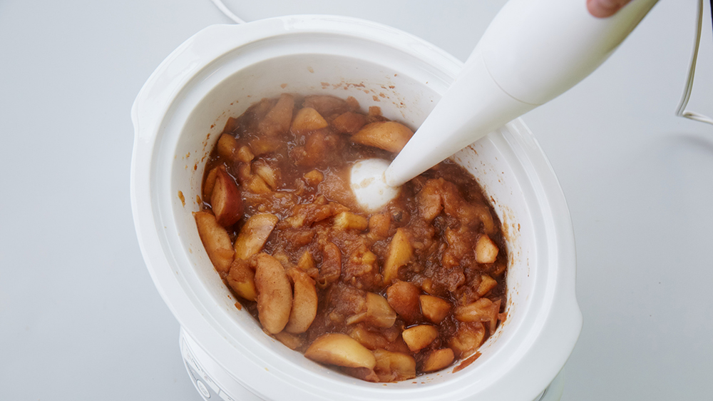 Cooked apples in a slow cooker with an immersion blender