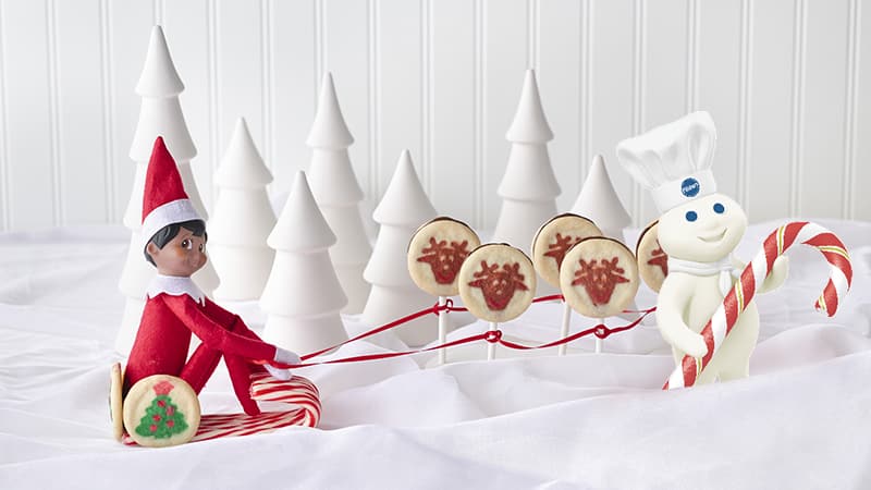 Elf on the Shelf  riding a cookie and candy cane sled with the Pillsbury Doughboy