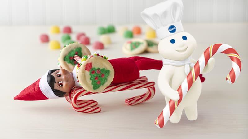 Elf on the Shelf with a weight bar made out of candy canes and cookies; the Pillsbury Doughboy with a candy cane