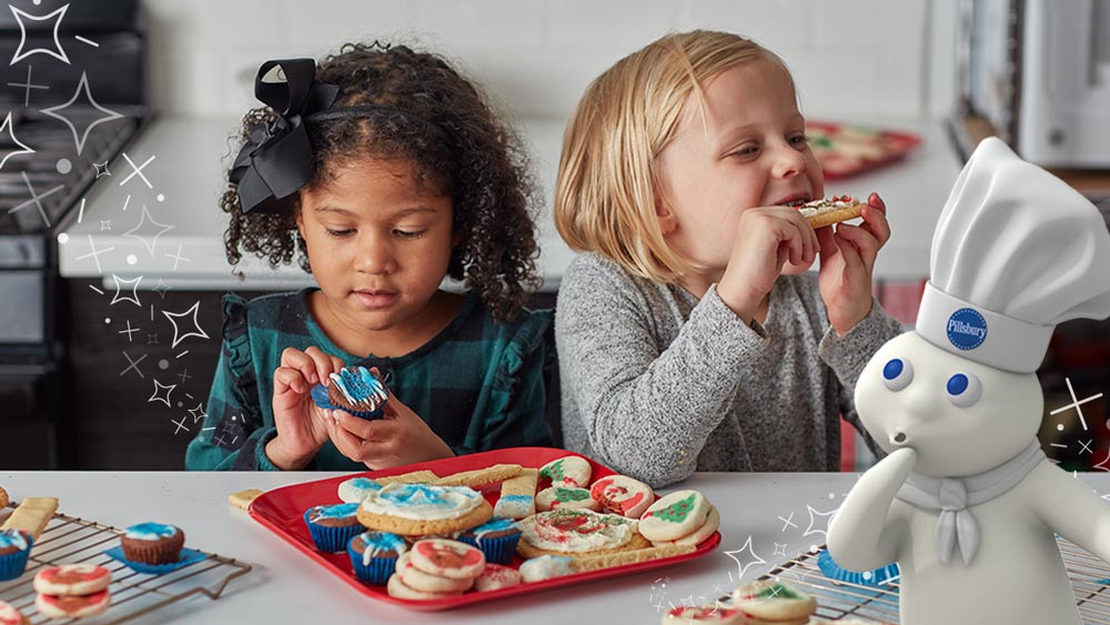 2 young girls eating Christmas cookies and the Pillsbury Doughboy