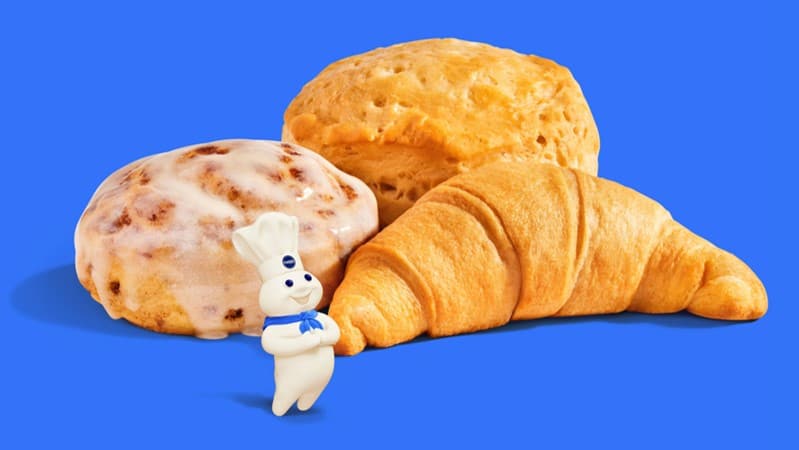 Croissant, biscuit, and cinnamon roll with the Pillsbury Doughboy on a blue background.